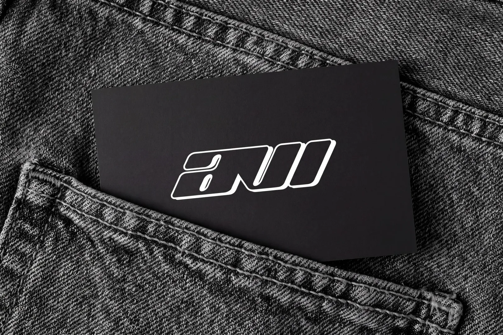 An AVI business card, the mark in white on black, tucked into the pocket of grey denim.